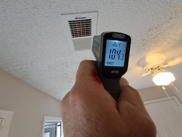 Hand holding an infrared thermometer pointing at a ceiling vent, displaying 101.3 degrees